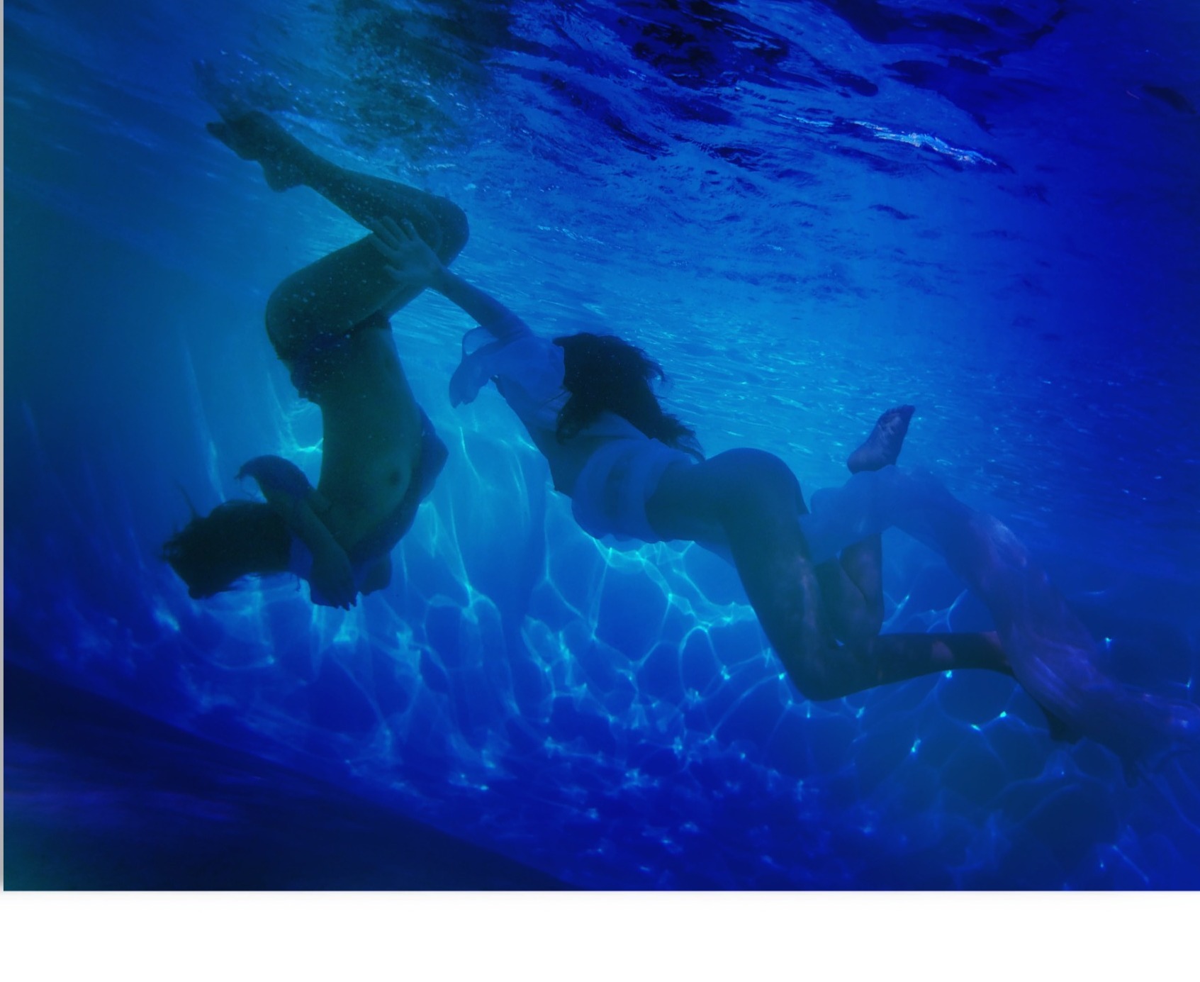 Swimmer descending through deep blue water